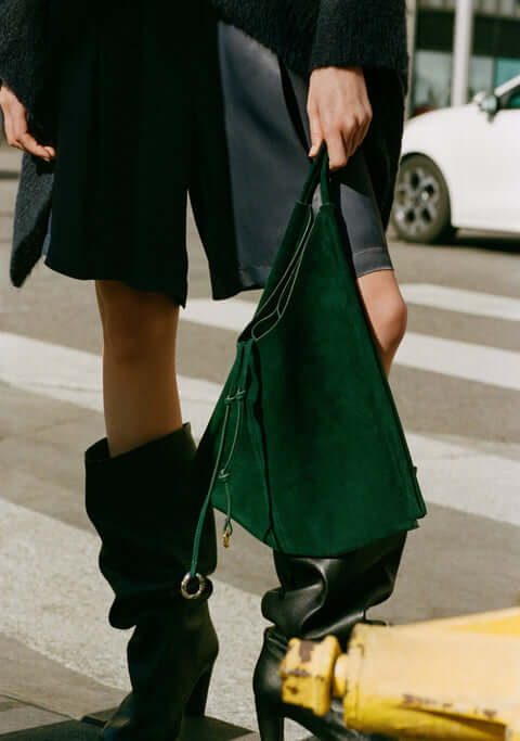 Street style women's fashion t-shirt outfit with black coat, knee-high boots and green suede handbag